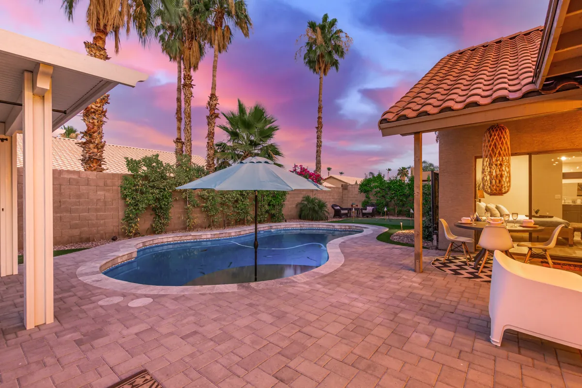 A serene backyard pool scene with palm trees, an umbrella, and outdoor seating. The space exudes relaxation and enjoyment, offering a private oasis for lounging after a day out at the park or preserve.