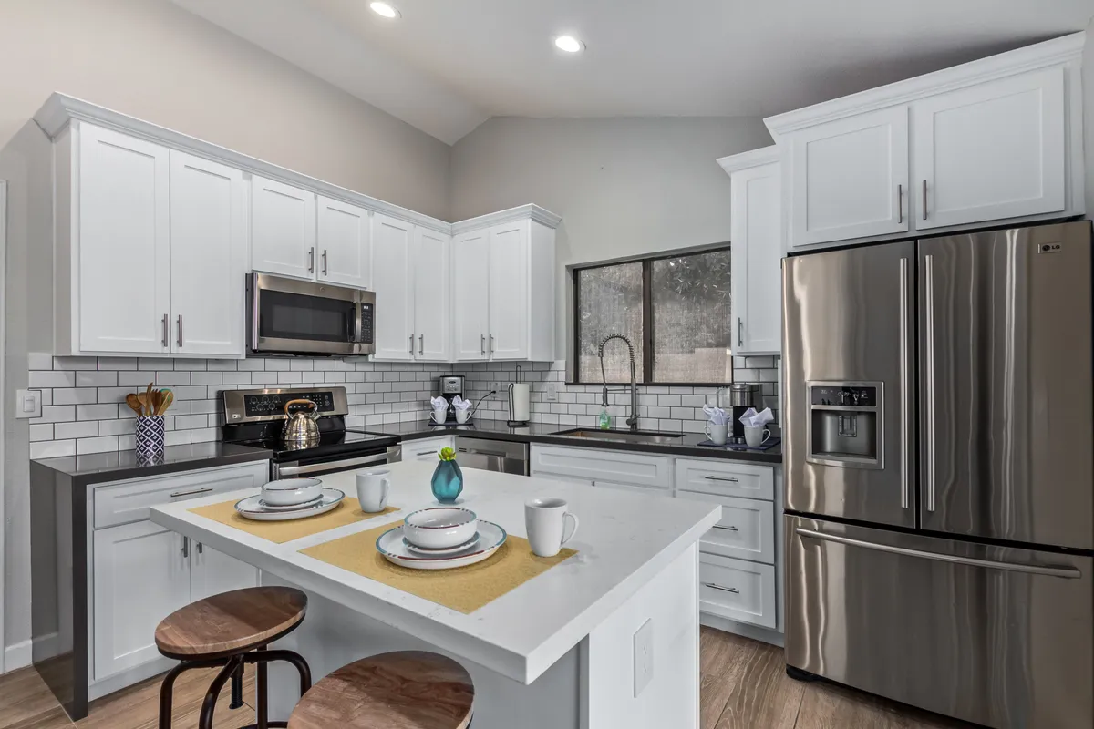 A modern, fully updated kitchen with a central island countertop, stainless steel appliances, white cabinetry, and tasteful decorative dishware. The kitchen exudes a welcoming and contemporary vibe, perfect for cooking and entertaining.