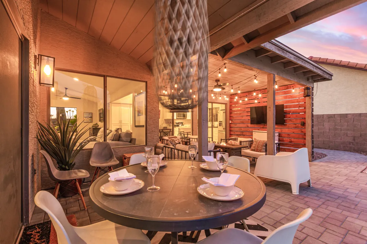 This image captures a welcoming outdoor dining area with a table set for a meal, cushioned seating, a decorative wooden wall, and a hanging light fixture, all designed for al fresco gatherings. The scene exudes a casual, social atmosphere, hinting at memorable evenings spent under the stars with friends.