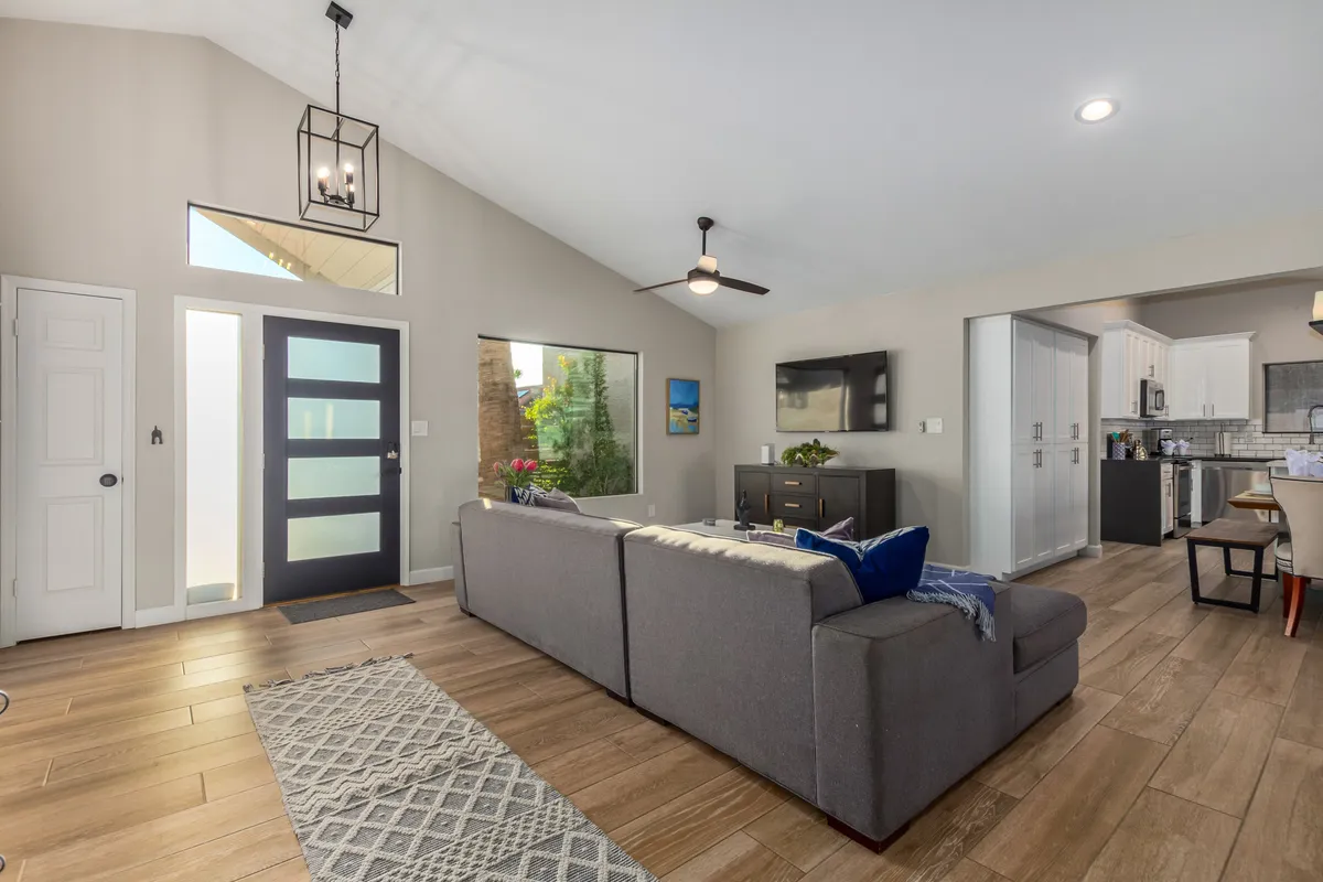 A cozy interior with a plush sofa, entrance door, windows, kitchen area, and a television. The setup is ideal for relaxing, entertaining, or enjoying family time in comfort.