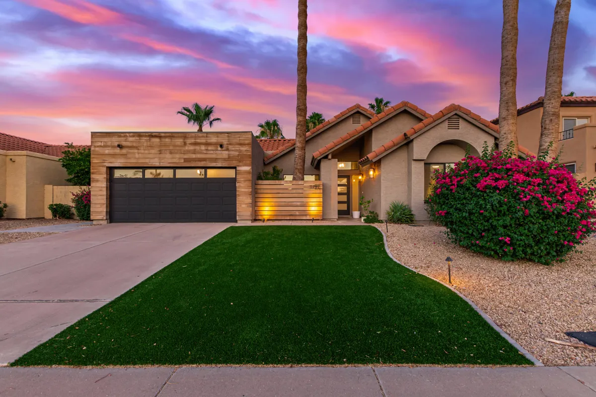 A welcoming exterior shot of the home with a modern garage door, landscaped front yard, palm trees, and blooming bougainvillea. The view suggests a neighborhood perfect for walks and evening strolls, connecting the home to its pet-friendly surroundings.