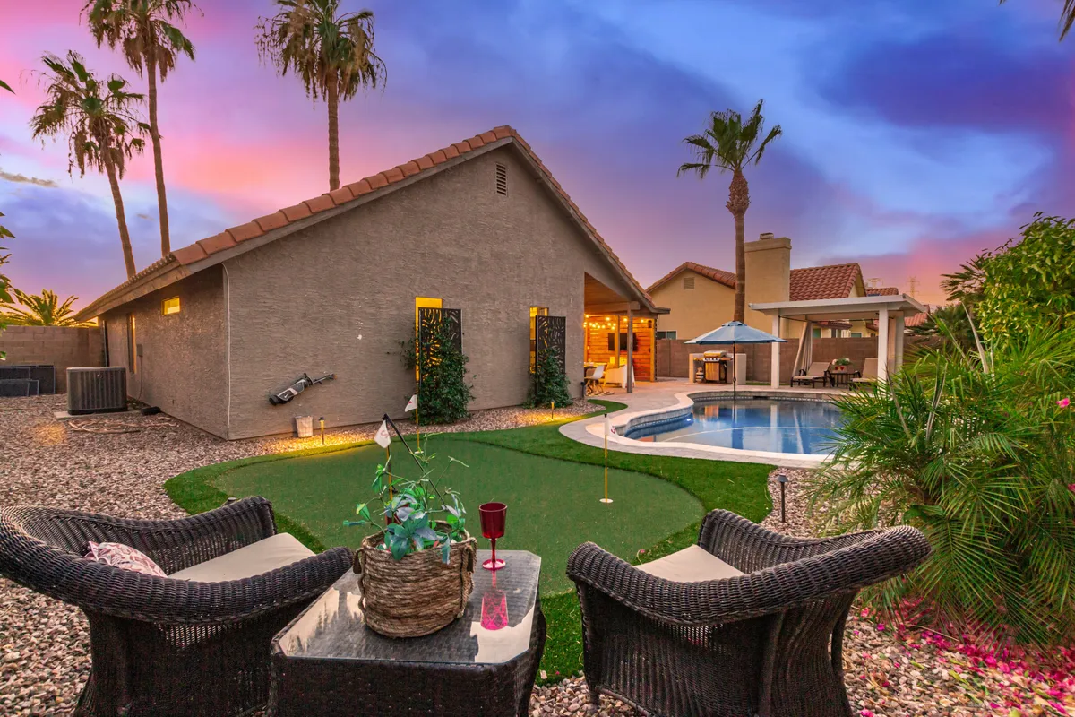 A serene backyard view highlighting the swimming pool, outdoor seating area, beautifully landscaped garden, and tall palm trees. The tranquil setting is perfect for relaxing after a day of exploration or hosting memorable summer nights.