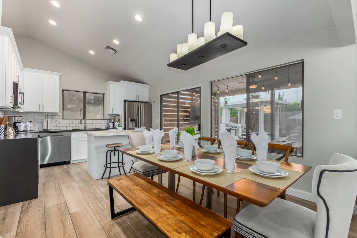 A dining table beautifully set for a meal, illuminated by a modern light fixture, with a view into the adjacent kitchen area. The setting is warm and inviting, perfect for family meals and entertaining guests.