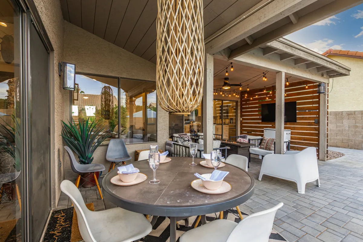 This image features another outdoor dining scene with a spacious table, hanging lights, lush potted plants, and a decorative wall, perfect for festive gatherings. The setup encourages both daytime brunches and evening get-togethers.