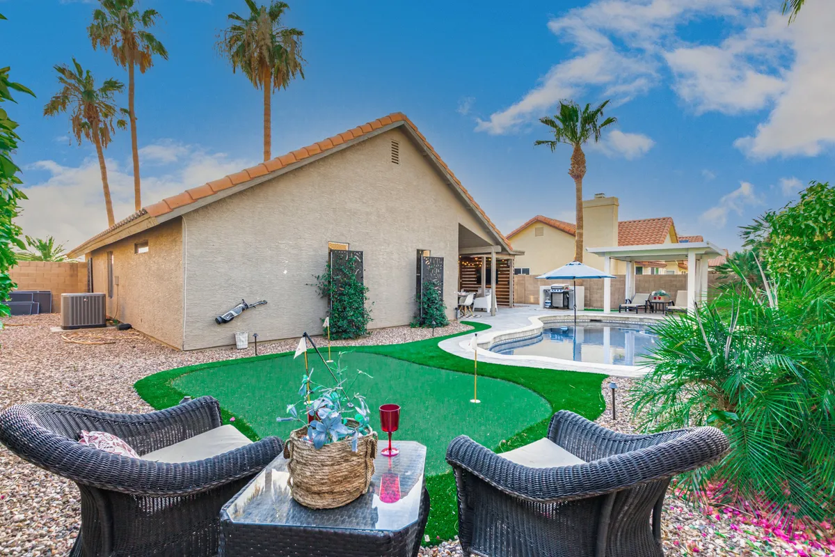 The photo captures a well-manicured backyard that includes both a pool and a golf putting green, along with palm trees and an inviting outdoor seating area. The ambiance is tranquil and perfect for socializing or practicing golf in the sun.
