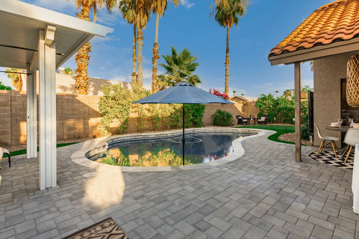 The photo showcases a sparkling swimming pool surrounded by palm trees, comfortable outdoor seating, and a large umbrella, creating an inviting oasis ideal for relaxing, swimming, or celebrating with friends.