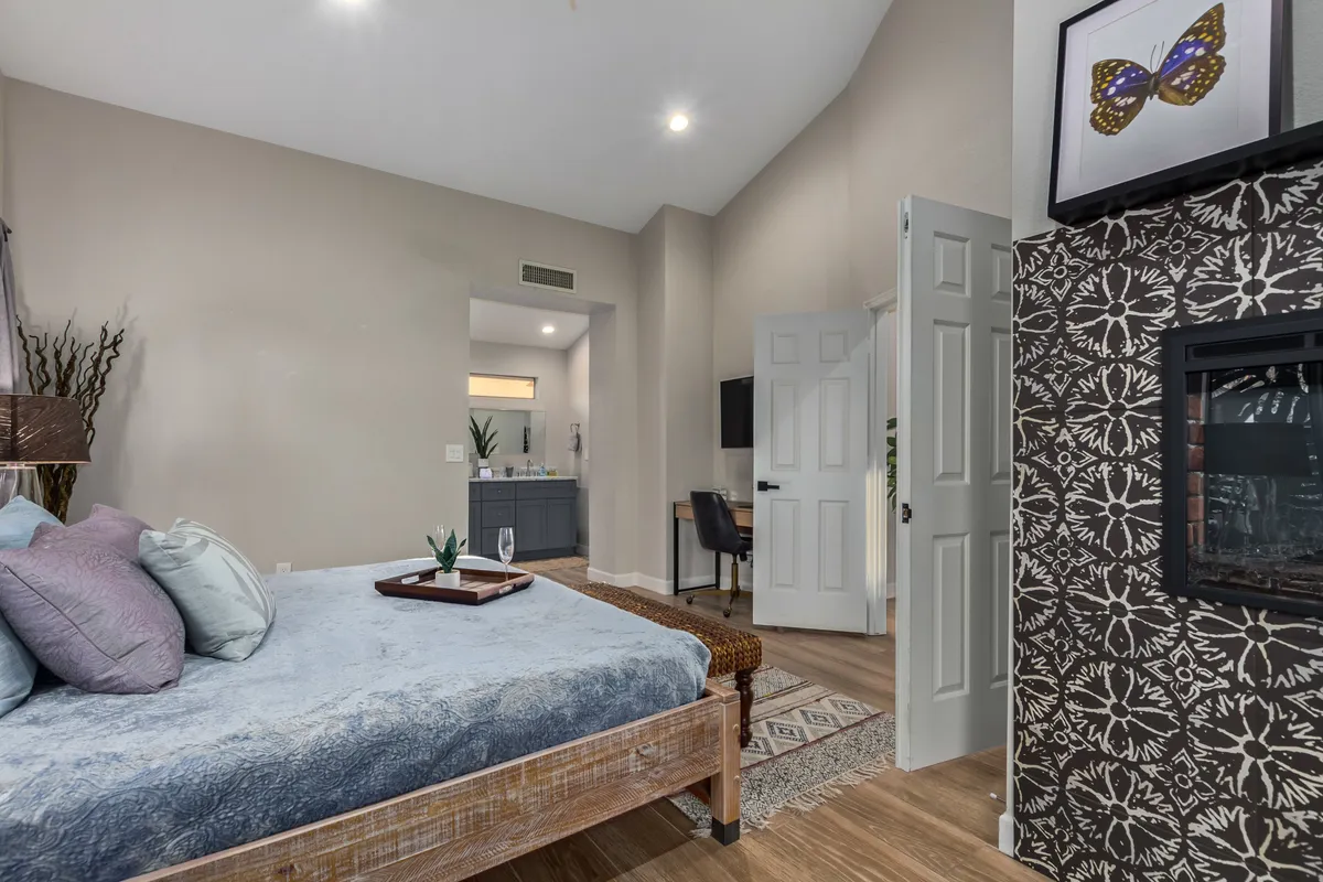A serene bedroom featuring a plush bed adorned with decorative pillows, a cozy fireplace below a piece of wall art, and soft, ambient lighting. The atmosphere is tranquil and inviting—perfect for unwinding after an active day.